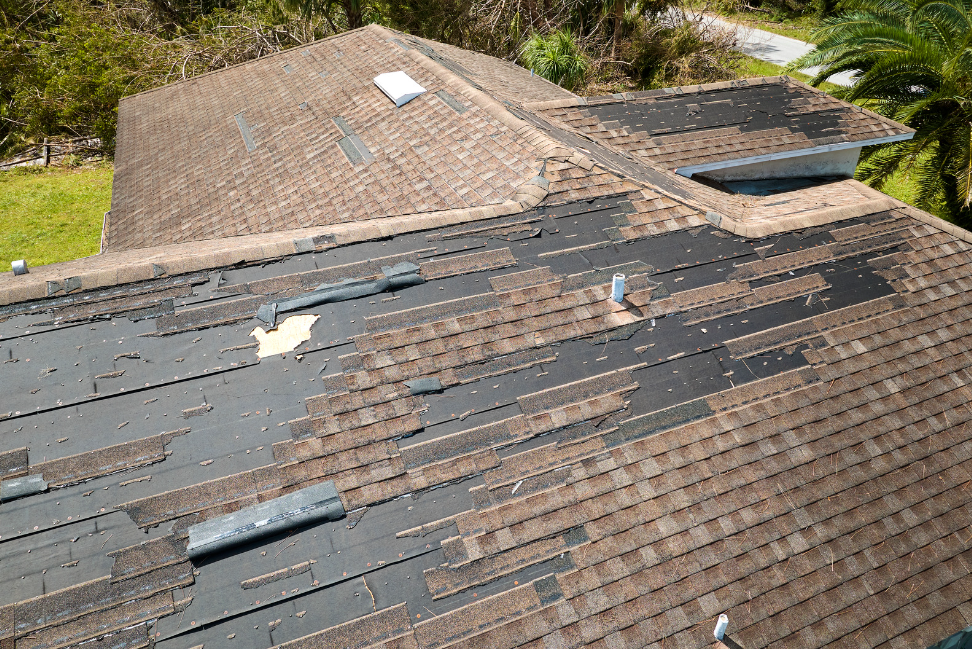 Damaged house roof with missing shingles after wind damage roof